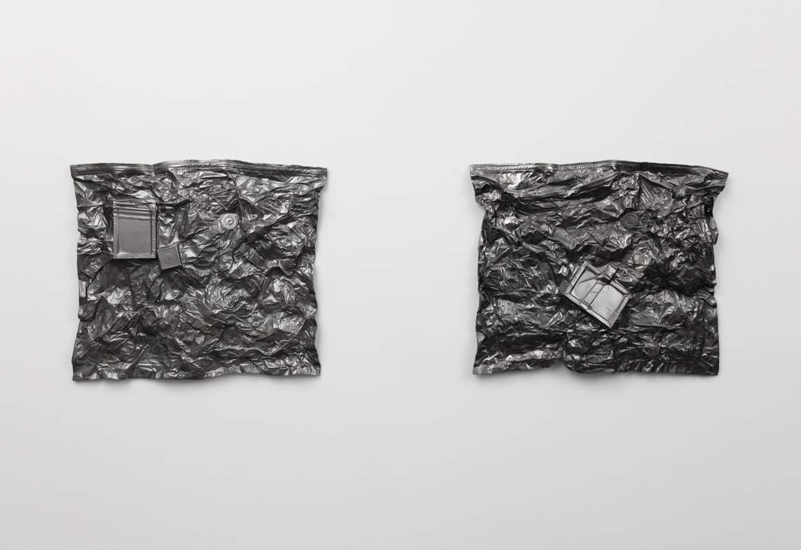 Rectangular objects and round vacuum seal air valves press out from textured backgrounds on these two almost square cast sculptures, which are colored shiny charcoal gray. The remaining surfaces are craggy and amorphous, like choppy water or cooling lava.