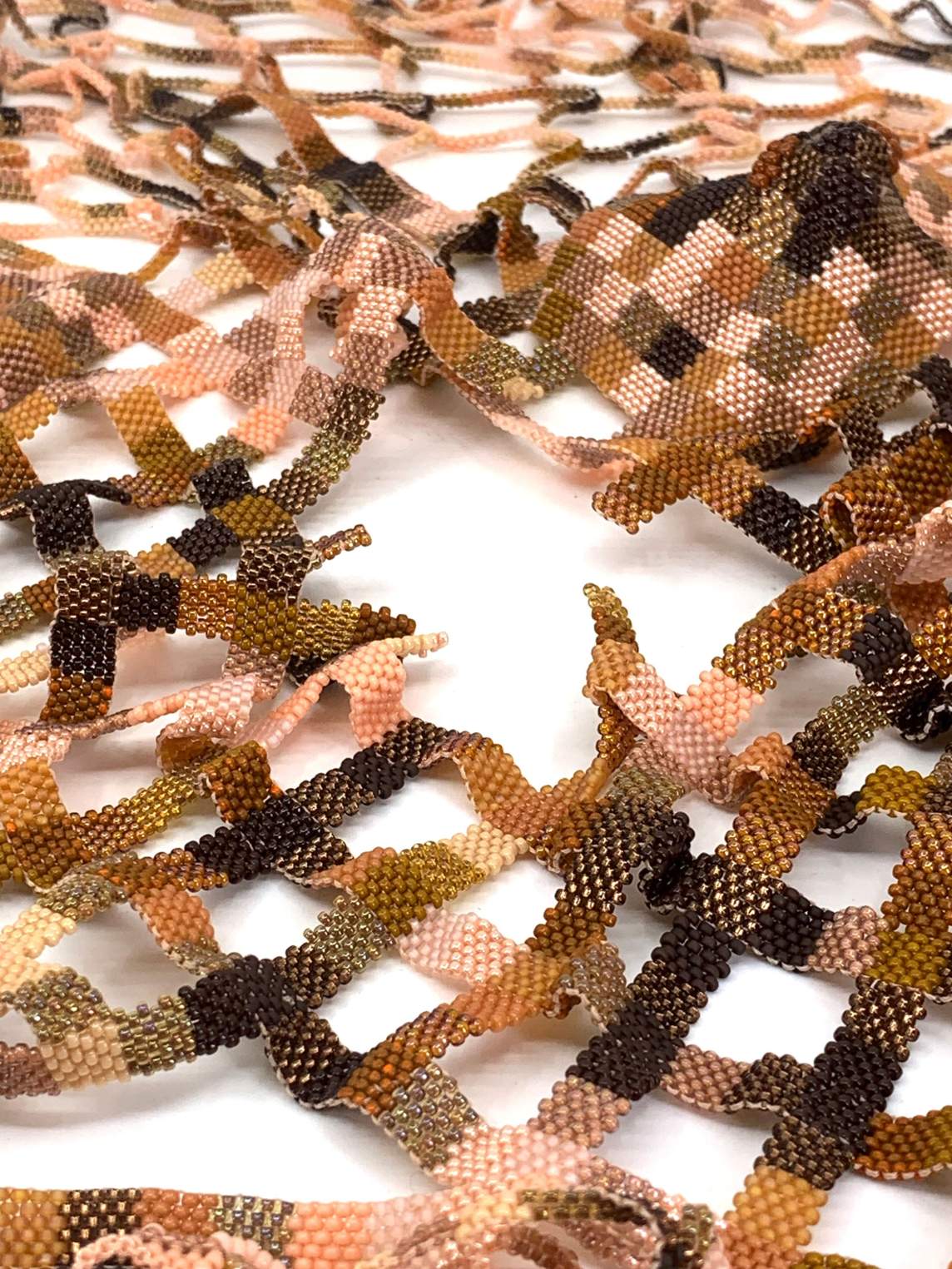 Close-up of what appears to be woven strips but turns out to be one continuous beaded grid. The colors range from shell pink to copper, bronze, iron, and black.