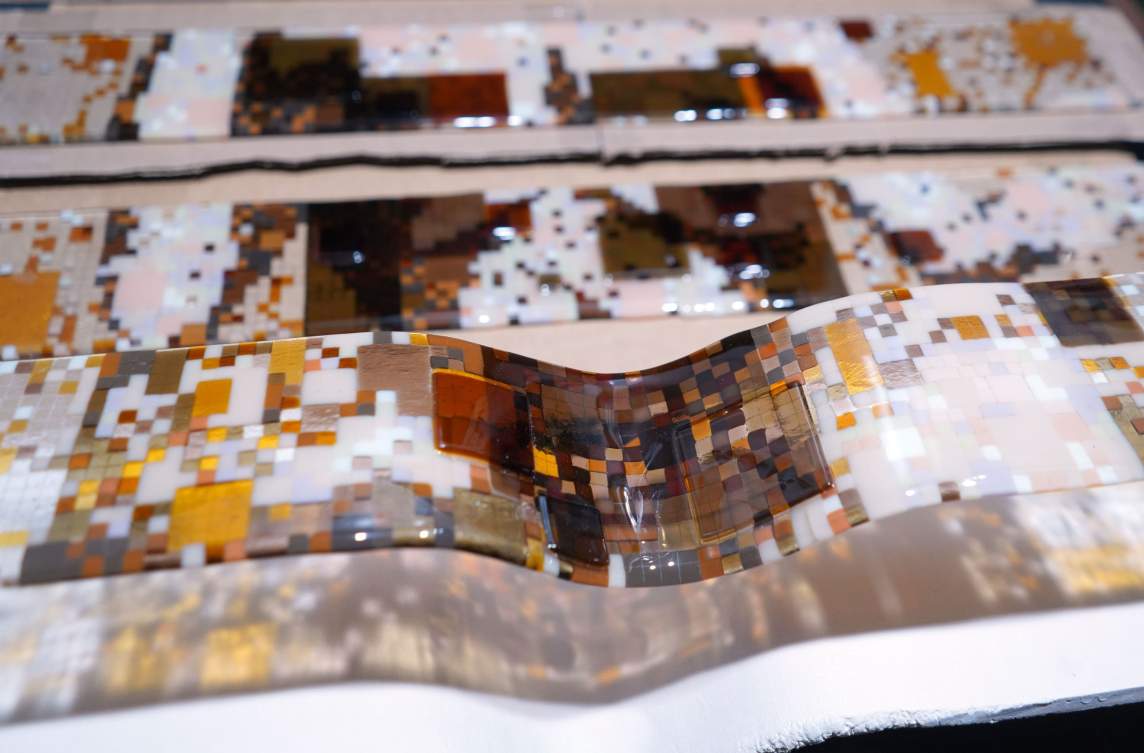 Close-up of what appears to be tiny squares of glass fused into strips. The minuscule squares are golden and butterscotch yellow, pearl and flat white, patina brown, and black.