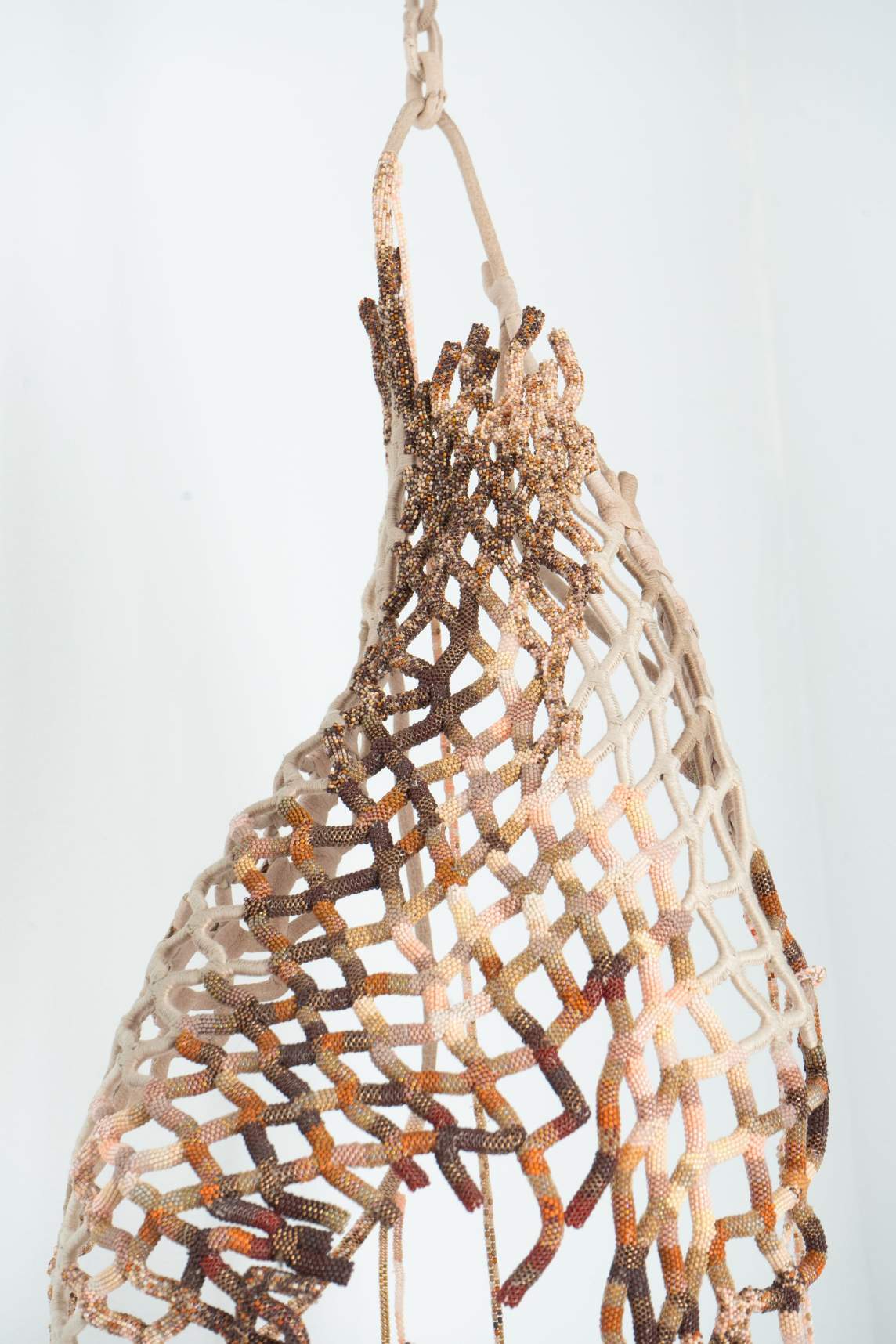 Close-up of the loose basket of soft parts shows that what appeared to be strips are wrapped with white thread except where the piece darkens around the hole. These latter areas are beaded in shades of brown, pink, and white.