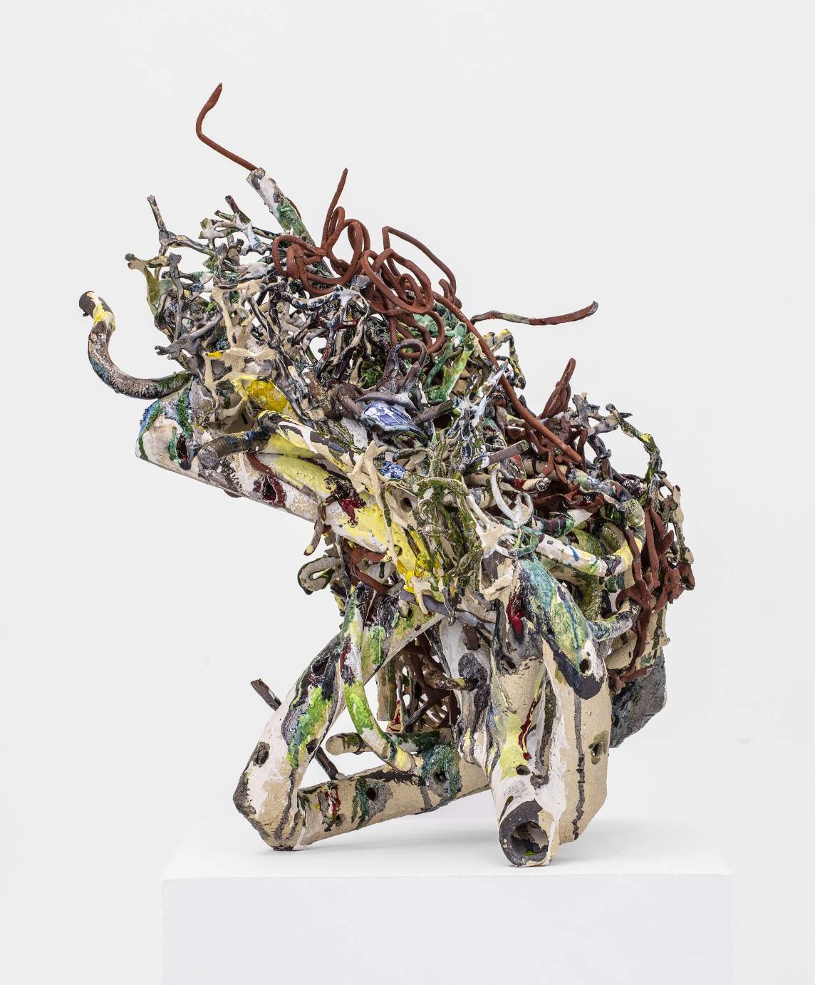 Pløen is an abstract ceramic sculpture with a base of arcing and bent ceramic tubes splattered with glaze, topped with thin forms of ceramic tangles that jumble and arc upwards in reds, browns, and greens, with embedded broken shards of European blue and white pottery.