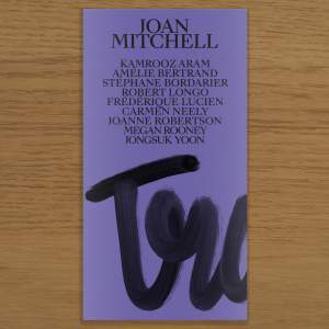 A narrow book with a purple cover lays on a wood table, the cover reads: “Joan Mitchell, Kamrooz Aram, Amelie Bertrand, Stephane Bordarier, Robert Longo, Frederique Lucien, Carmen Neely, Joanne Robertson, Megan Rooney, Jongsuk Yoon” Below the names is a partial word scrawled in vertical cursive reading “Tra”