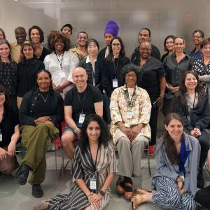 A group of people of various age, dress, and appearance stand and sit in a posed group, smiling.