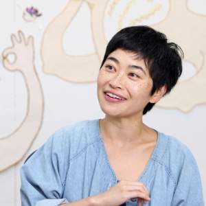 Cindy Cheng smiles in front of artwork, she is an Asian-American woman with short dark hair and light skin tone.