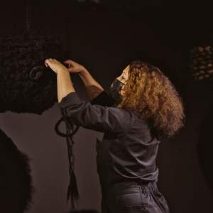 Angela Hennessy in a dark gallery space adjusting a sculpture