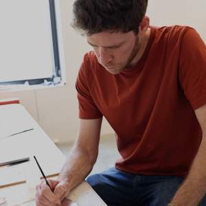 Joshua Mintz, a white man with short dark hair and beard, paints onto miniature bricks in an art studio.