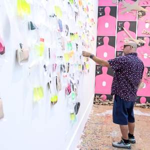 Garvin Sierra, a Puerto Rican man with a shaved head, glasses and medium skin tone, adjusts a component of an installation on a studio wall.