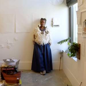 Artist Asante Salaam leaning against a studio wall with various papers pinned up