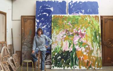 Artist Joan Mitchell leaning on a stool in front of 2 large paintings