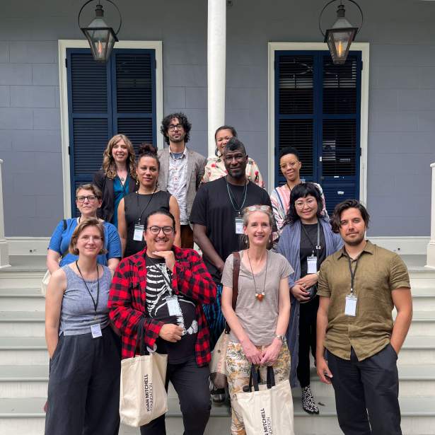 A group of 12 people of various age and dress stand on the steps of the porch of the Joan Mitchell Center