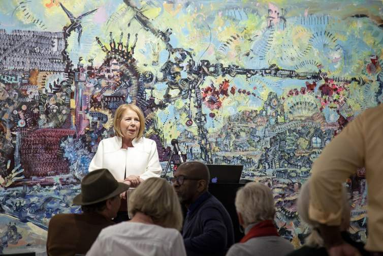Michele Tortorelli speaking to a seated audience in front of a large artwork