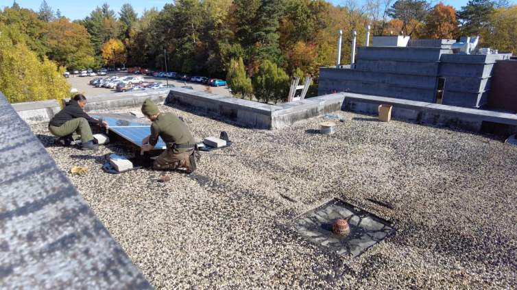 On a flat graveled roof, two people work on a solar array.