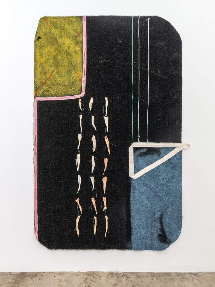 A field of black Astroturf forms a rectangular shape with rounded corners, punctuated by 3 columns of corn husks marking down the center-left of the piece. At the upper right is a painted yellow rectangle, framed by pink yarn that then follows down the length of the piece, and at the opposite corner is a light blue rectangle with a right triangle framing a corner with frayed canvas.