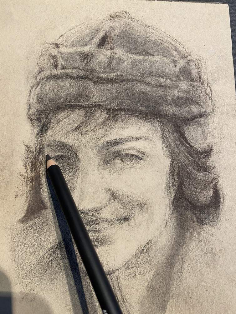 A pencil is shown on paper, creating a sketchy drawing of a woman's smiling face. She has short hair and wears a pointed skullcap hat.