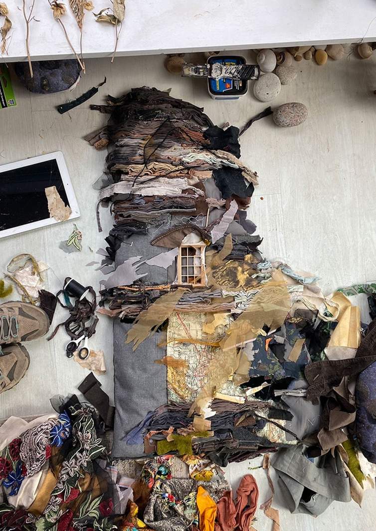 Resting on the floor of Ruby Chishti's studio, a sculptural composition of a house is created with layers of fabric that create a striated composition.