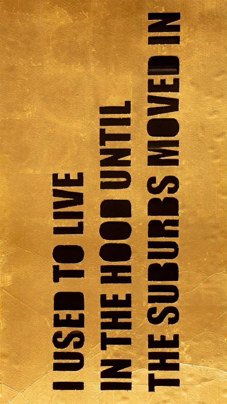 A detail of an artwork with gold leaf on cardboard and letters cut out that read "I USED TO LIVE IN THE HOOD UNTIL THE SUBURBS MOVED IN"