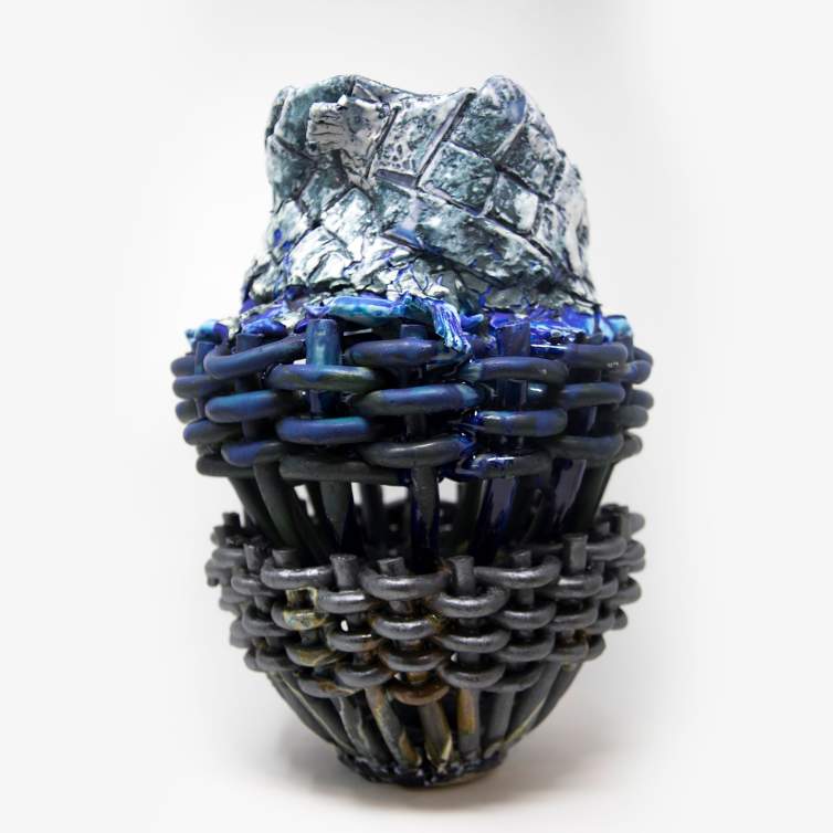 A ceramic sculpture created from three sections of coiled and woven clay, to create an open basket-like form. The sculpture is finished with whitish-green-blue glaze on top, flat blue glaze in the middle, and metallic brown glaze on the bottom section.