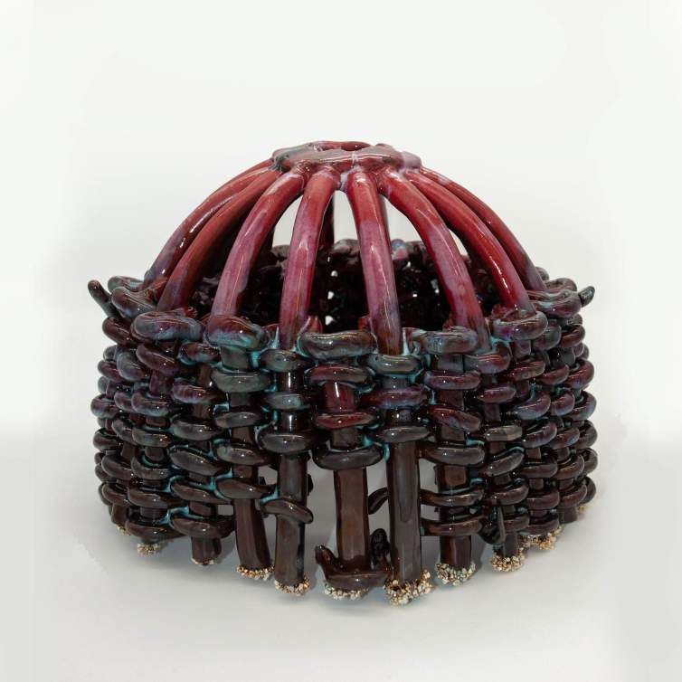 A ceramic sculpture formed with coils of clay that create an arched framework, interwoven with smaller coils below in a basket-weaving pattern. The piece is finished with a raspberry pink glaze on top that transitions into darker blue and brown tones near the bottom.