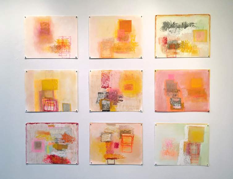 A grid of 9 abstract drawings with bright colors are pinned to a white wall. The drawings repeat and overlay squares, scribbled gestural lines, and gauzy smudges in shades of yellow, orange, ochre, pink, and magenta.