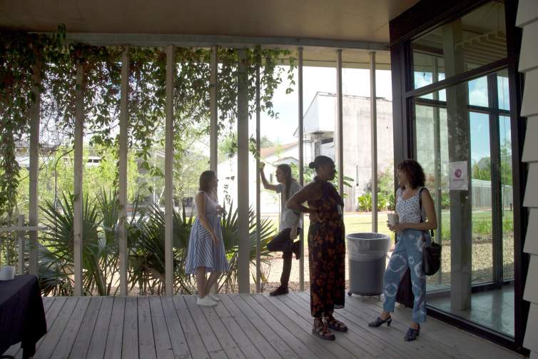 People stand on a porch area with vertical bars and hanging greenery.