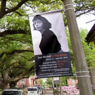 A banner on a streetlight advertises "Joan Mitchell in New Orleans" exhibitions with a photo of Joan Mitchell