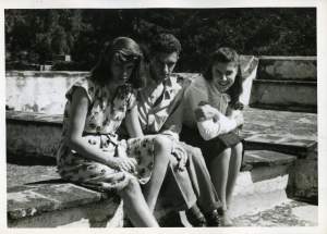 3 young people with light skin tone sit on a bench smiling