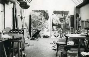 A dog sits in front of a large abstract diptych in an art studio