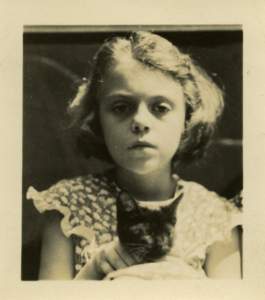 A young white girl with a serious expression holding a dark kitten