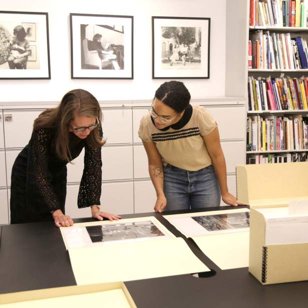 Two women lean over a table inspecting photographs in archive folders