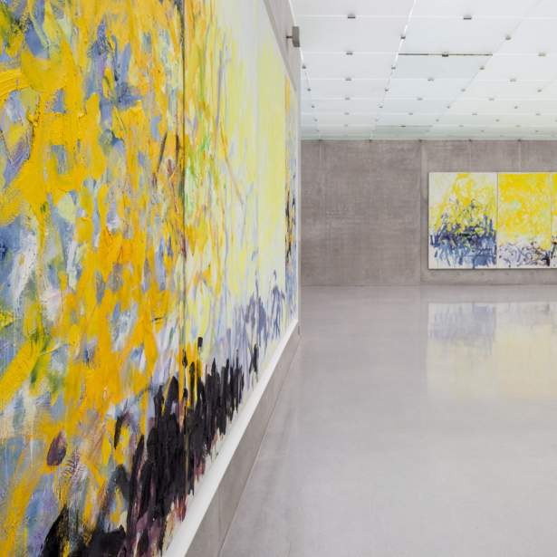 Two large abstract yellow and blue paintings by Joan Mitchell hang in a large gallery space with concrete floors and walls