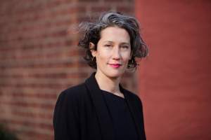 Solana Chehtman, a Latinx woman with curly black and grey hair and a slight smile, wearing a black blazer in front of brick wall
