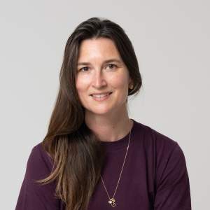 Mara Hoberman smiles warmly. She is a white woman with long brown hair wearing a purple sweater and gold chain.