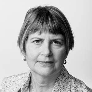 Schimert in black and white wears a floral print collared shirt, with filigree necklace and earrings. She has short medium tone hair and light skin.