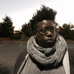 Nyeema looks off to the side, wearing glasses and a thick gray scarf. She has dark skin and short dark hair with tight upward curls.