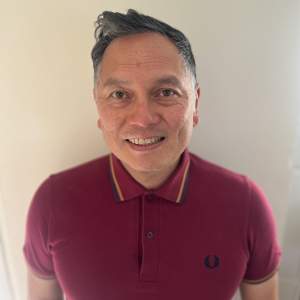 Michael Arcega is a Filipino man with short, dark hair. Smiling at us, he wears a red polo shirt buttoned all the way up.