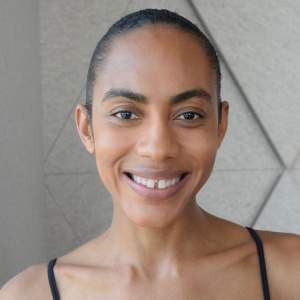 Dillon is a Black woman with black hair slicked back. She wears a black tank top and smiles warmly.