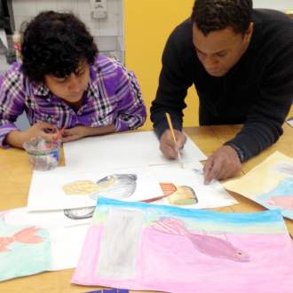 An artist teacher drawing on paper with a youth observing the technique