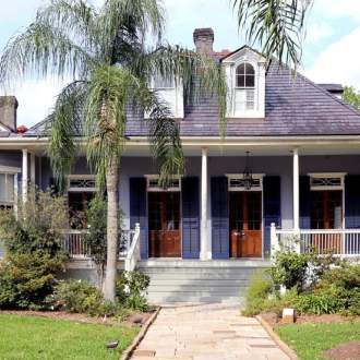 The main house of the Joan Mitchell Center, a blue creole cottage house with a large front porch and blue shutters