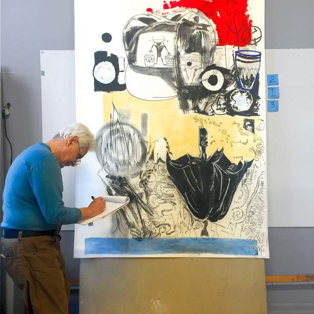 Marcos Dimas, a Puerto Rican man with medium tone skin, short gray hair and glasses, takes notes on a legal pad in front of a large artwork on paper.