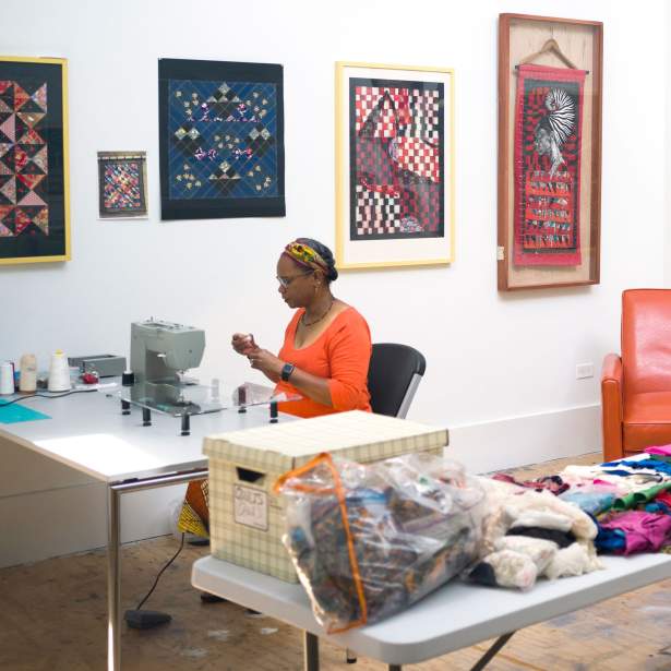 Artist Louise Mouton Johnson working at a sewing machine in her studio at the Joan Mitchell Center. She is surounded on the walls by patterned paper and fabric framed works.